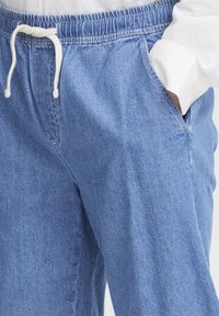 Pantalones jogger de denim azul claro con cintura elástica, cordón ajustable y bolsillos laterales. Presenta una tela suave y texturizada.