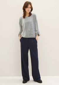 Grå mønstret bluse med vide ærmer, kombinert med marineblå brede bukser. Outfiten har en avslappet passform og subtil tekstur. Svarte sko fullfører looken.