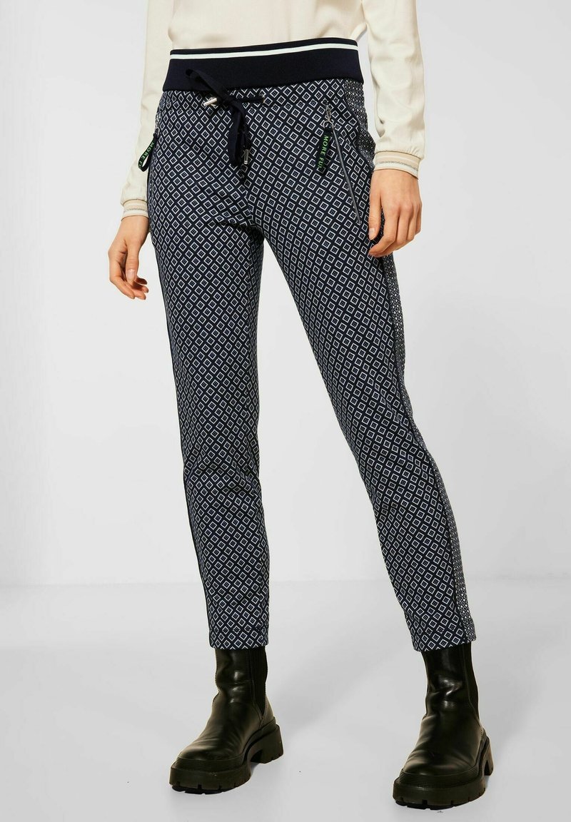 Marinblå byxor med geometriskt mönster, elastisk midja med dragsko, sidofickor och smal passform, kombinerat med svarta stövlar.