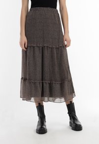 Gonna maxi in tessuto trasparente marrone con motivo floreale. Presenta volant a strati e una vita elasticizzata. Abbinata a stivali alla caviglia in pelle nera.
