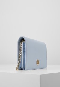 Jasnoniebieska skórzana torba na ramię z złotym łańcuszkowym paskiem, klapką na górze, wytłoczonym logo i teksturowaną powierzchnią. Kompaktowy i prostokątny kształt.