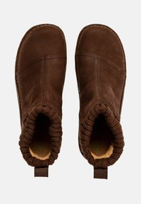 Par de botas de tobillo de cuero marrón sin cordones con puños de punto y tiradores, vistas desde arriba sobre un fondo claro.