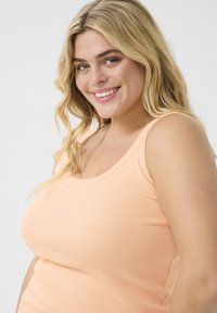 Peach ribbed tank top with wide straps and a round neckline, showcasing soft texture and form-fitting design.