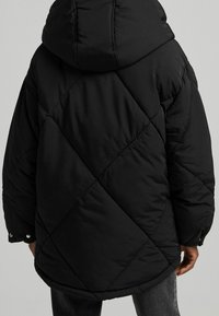 Czarna kurtka puchowa z kapturem, z pikowanym wzorem w diamenty, elastycznymi mankietami i detalami na zatrzaski. Miękka, gładka faktura materiału.