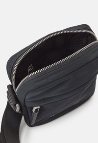 Schwarze rechteckige Umhängetasche aus strapazierfähigem Material, mit einem Reißverschlussöffnungs-, gestepptem Design und verstellbarem Tragegurt.