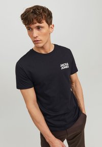 Schwarzes Baumwoll-T-Shirt mit Rundhalsausschnitt und kurzen Ärmeln. Auf der linken Brustseite befindet sich das weiße "JACK & JONES"-Logo.