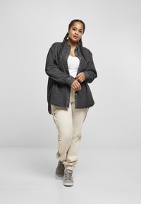 Svart denimskjorte med knappelukking, hvit tank top, beige cargo bukser og grå sneakers, står på en lys bakgrunn.