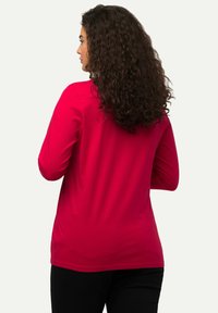 Langarm, leuchtend rotes Shirt aus weichem Stoff. Verfügt über einen lockeren Schnitt und eine glatte Textur, mit einem runden Ausschnitt und minimaler Ausgestaltung.