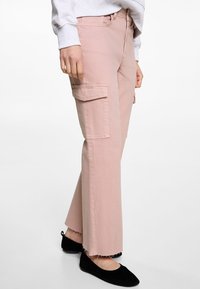 Světle růžové cargo kalhoty s rovnými nohavicemi, vybavené předními a bočními kapsami, neupraveným lemem a bavlněným materiálem. Nosené s černými balerínami.