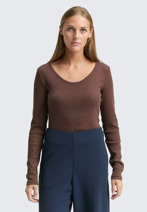 Braunes Langarmoberteil mit rundem Ausschnitt, aus geripptem Stoff gefertigt, kombiniert mit hoch taillierten marineblauen Hosen. Schlichtes, figurbetontes Design.