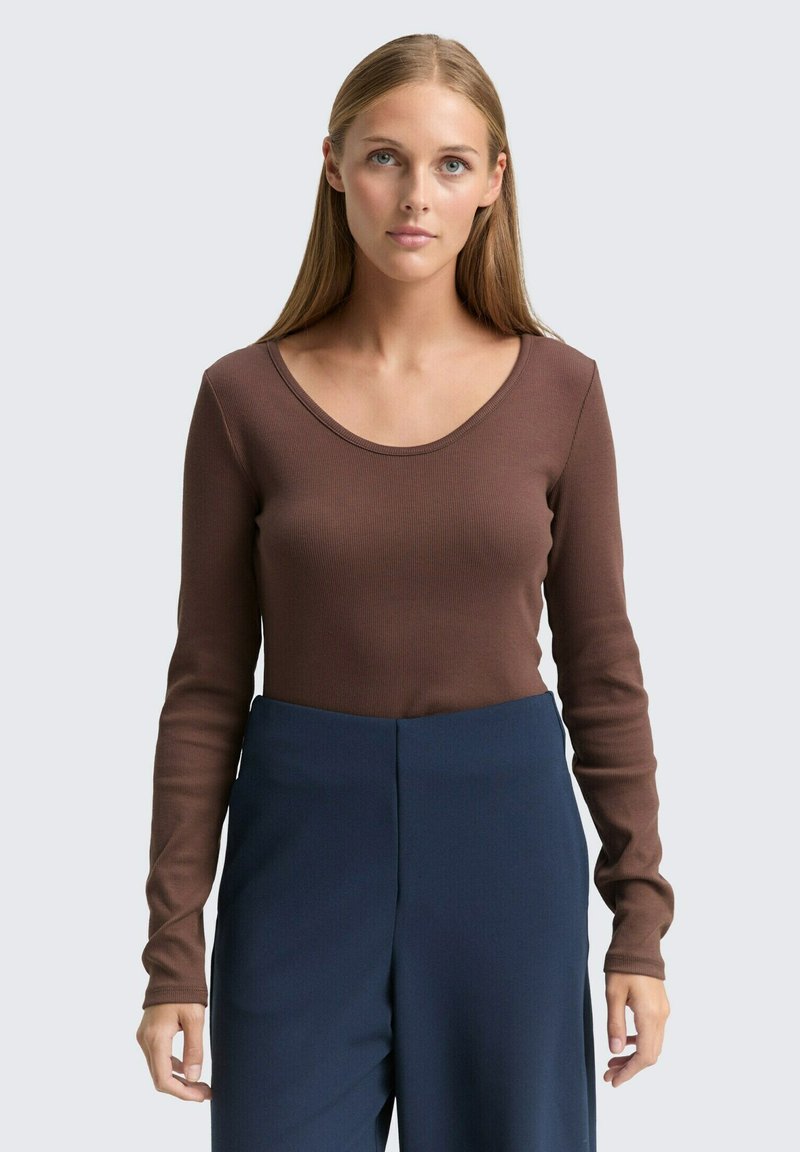 Braunes Langarmoberteil mit rundem Ausschnitt, aus geripptem Stoff gefertigt, kombiniert mit hoch taillierten marineblauen Hosen. Schlichtes, figurbetontes Design.