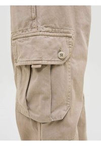 Beige cargobyxor i bomullstyg med en sidoficka som har knäppning och sydda detaljer. Texturen är slät med en lätt lyster.
