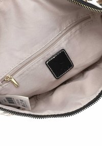 Interno di una borsa con zip, caratterizzato da tessuto beige, un piccolo etichetta nera e una tasca sicura con una zip dorata. Finiture testurizzate lungo i bordi.