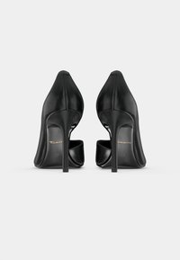 Chaussures à talons hauts noires en cuir lisse et élégant, à bout pointu et avec un talon stiletto mince. Logo de marque discret sur la semelle intérieure.