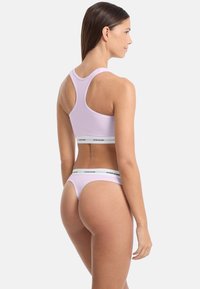 Paarse katoenen sportbeha met een racerback ontwerp, gecombineerd met een bijpassende lage thong met een witte band waarop de tekst "GUESS JEANS" staat.