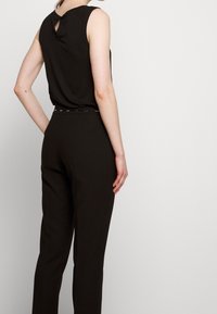 Černý bezrukávový top s detailem klíčové díry na zadní straně, spárovaný s černými kalhotami s vysokým pasem a slim fit, které mají jemnou texturu.