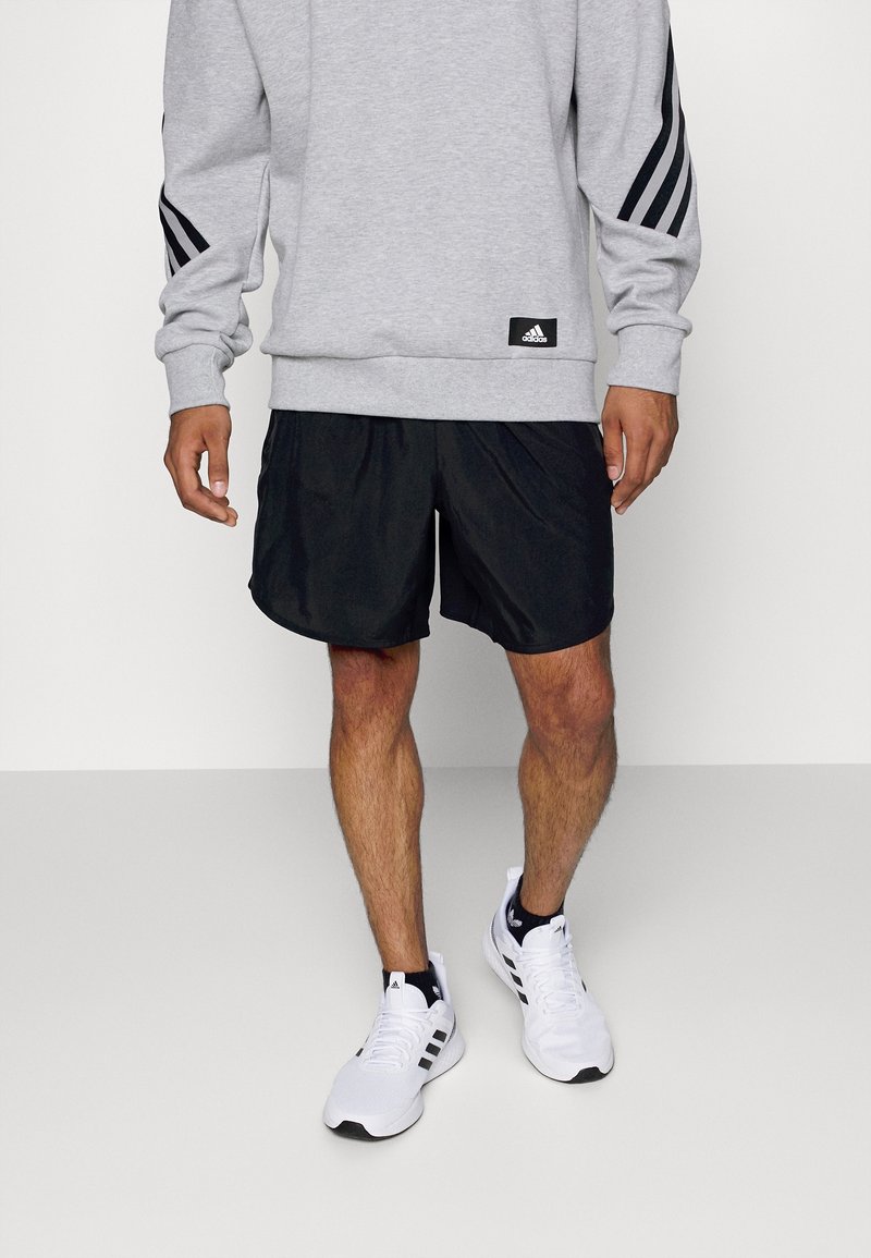 Grå sweatshirt med svarta randdetaljer, ihopparad med svarta träningsshorts. Vita sneakers med svarta detaljer fulländar outfiten.