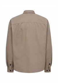 Chemise à manches longues, boutonnée, en tissu de couleur marron clair. Elle présente un col, une empiècement au dos, des plis aux épaules et des poignets à boutons. Texture lisse.