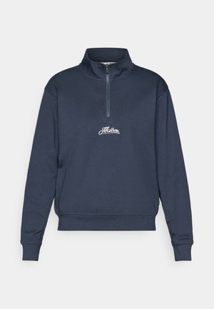 Hanorac cu fermoar de culoare albastru marin, fabricat dintr-un material moale. Are un guler înalt, mansete cu nervuri și un logo brodat pe piept.