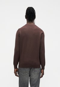 Brown knitted sweater with long sleeves and a crew neck. Soft texture, fitted design, and minimalistic detailing at the hemline and cuffs.