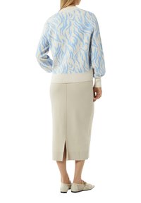 Hellblau-weiß gemustertes Sweatshirt mit geripptem Saum, kombiniert mit einem beigen Midikleid mit Rückenschlitz und beigen Netzschuhen.