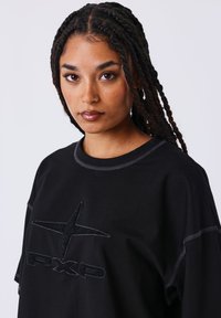 T-shirt nera oversize in cotone con cuciture a contrasto. Presenta un logo testurizzato con design a stella sul davanti.