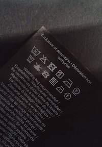 Étiquette d'entretien en tissu noir avec instructions de lavage, symboles pour le lavage, le séchage et le repassage ; texte imprimé en plusieurs langues, visibilité claire.