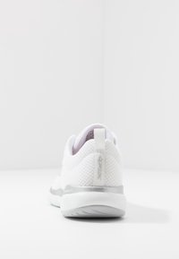 Vit nät-sneaker sedd bakifrån, med en grå sula och dragflik med en subtil logotyp på en vit bakgrund.