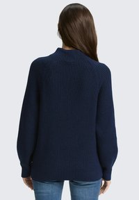 Marineblauwe geribde trui met een hoge kraag en lange mouwen, met een relaxed fit en een drop shoulder ontwerp. Zachte textuur zichtbaar.