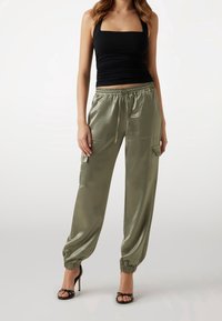 Satijnen olijfgroene broek met een elastische tailleband, zijzakken en omgeslagen zomen, gecombineerd met een nauwsluitend zwart topje. Zwarte sandalen met hoge hak.