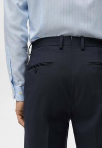 Granatowe spodnie z dwoma tylnymi kieszeniami, ozdobione czarną lamówką i guzikowym akcentem. Połączone z jasnoniebieską koszulą w paski.