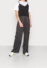 Černý top s krajkovým lemem přes bílém tričku, doplněný černobílými pruhovanými cargo kalhotami s mnoha kapsami. Nosené se sneakerami.