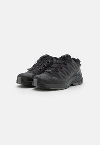 Black athletic shoes with a textured upper, laces, and reinforced toe cap. Features a rugged outsole for traction and stability.