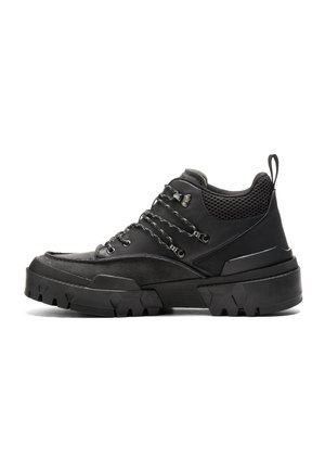 Schwarzer robuster Wanderschuh mit dicker Stollenlaufsohle, gepolstertem Netzkragen, Metallösen und Zuglasche an der Ferse.