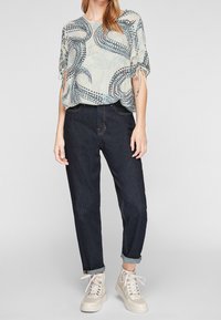 Blouse bleu clair avec un motif tourbillonnant, coupe ample et manches courtes. Associée à un pantalon en denim foncé et des baskets beiges.