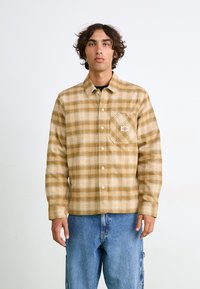 Ternede, varmtonede flannel skjorte med en brystlomme, knapper og et logo-patch. Sammen med lyse denimbukser.