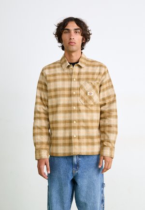 Chemise en flanelle à carreaux aux tons chauds, avec une poche poitrine, des boutons et un patch logo. Associée à un pantalon en denim clair.