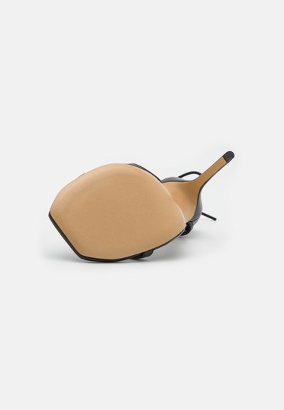 Zapato negro de tacón alto con punta afilada y suela beige, mostrado desde la vista inferior con una textura lisa y un diseño minimalista.
