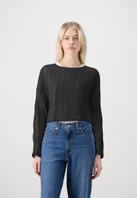 Zwart cropped langemouwen top met ribbeltextuur, gecombineerd met hooggewaadde blauwe jeans. Eenvoudige ronde halslijn en lichte transparantie.
