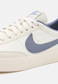 Vita lädersneakers med en strukturerad yta, ljusblå detaljer och en gummisula. Har runda snören och en blå logotyp på tungan.