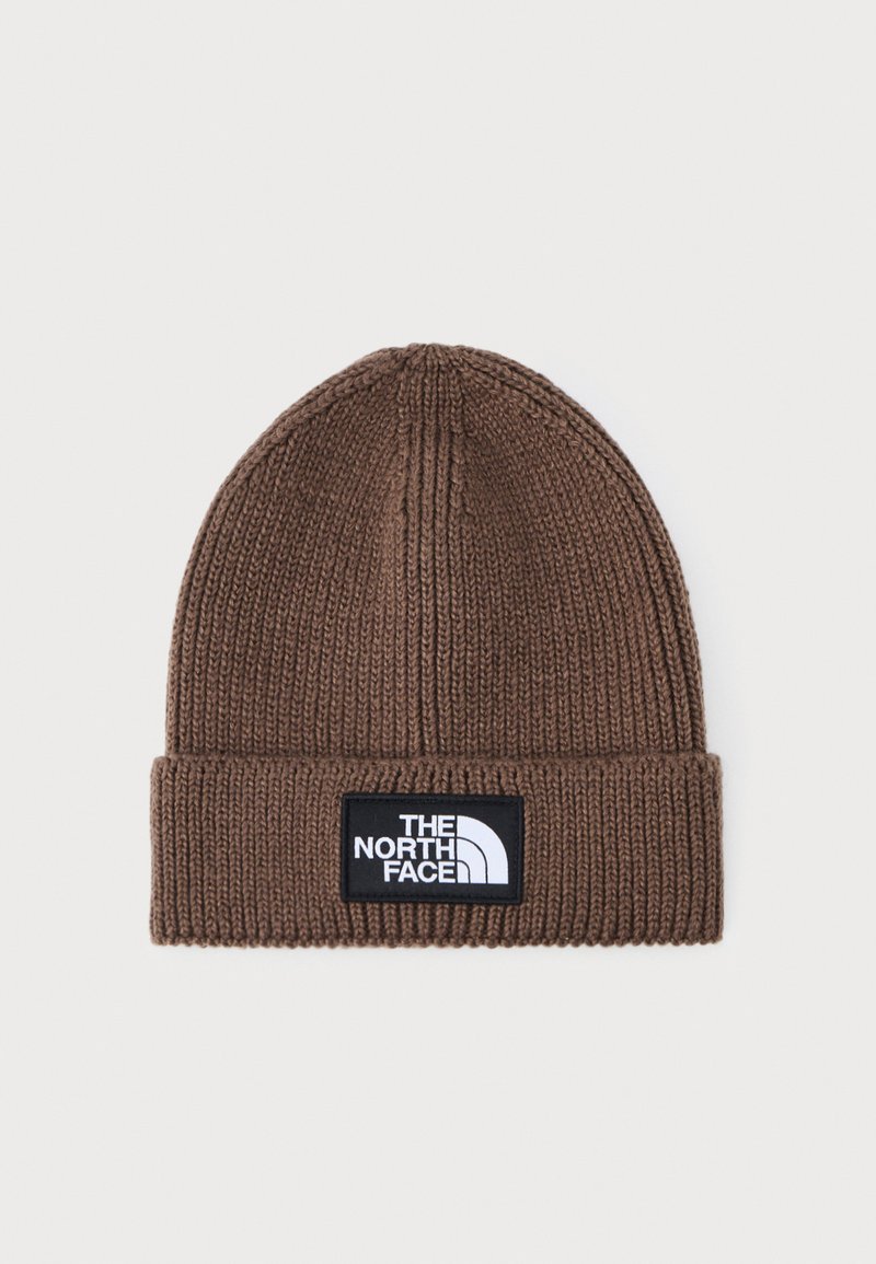 Gorro de punto marrón con textura acanalada y puño doblado. Presenta un parche rectangular negro con texto de logo en blanco.