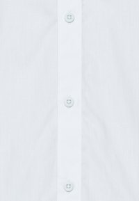 Bílá košile na knoflíky s hladkou texturou, vybavená pěti světle modrými knoflíky a středovým klopou. Jednoduchý design bez vzorů nebo ozdob.