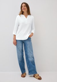 White, textured top with a henley neck and three-quarter sleeves, paired with light blue, wide-leg jeans and tan sandals.