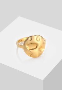 Guld ring med et rundt, tekstureret ansigt med udskårne former, sat på en glat ring. Overfladen reflekterer lyset, hvilket skaber en blank finish.