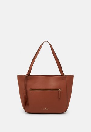 Sac fourre-tout en cuir marron avec une poche zippée à l'avant, un détail de pampille et des doubles bretelles, sur un fond gris clair.