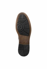 Semelle en caoutchouc brun avec sections noires texturées et un motif circulaire. Présente des stries et des motifs variés pour l'adhérence et la traction.