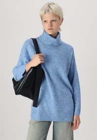 Pull à col roulé surdimensionné bleu clair en tissu tricot doux, associé à un sac en cuir noir avec une longue bandoulière. Jean délavé.