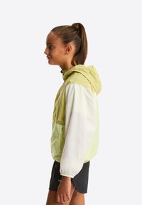 Hættetrøje med vindafvisende materiale i et farveblokdesign med lys limegrøn og hvid. Har elastiske manchetter og en forlomme. Glat stoftekstur.