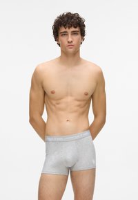 Szürke boxer alsónadrág puha anyagból, márkázott derékpánttal és szívlogóval az elején. A modell laza pózban áll.