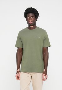 T-shirt en coton olive avec col rond, manches courtes et texte logo blanc sur la zone de la poitrine gauche. Texture lisse, coupe classique.